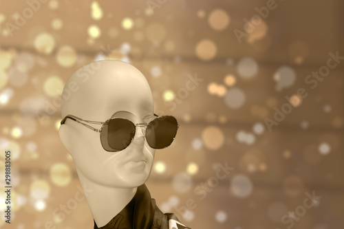 Mannequin head in sunglasses, muted color beige brown backdrop background bokeh shine