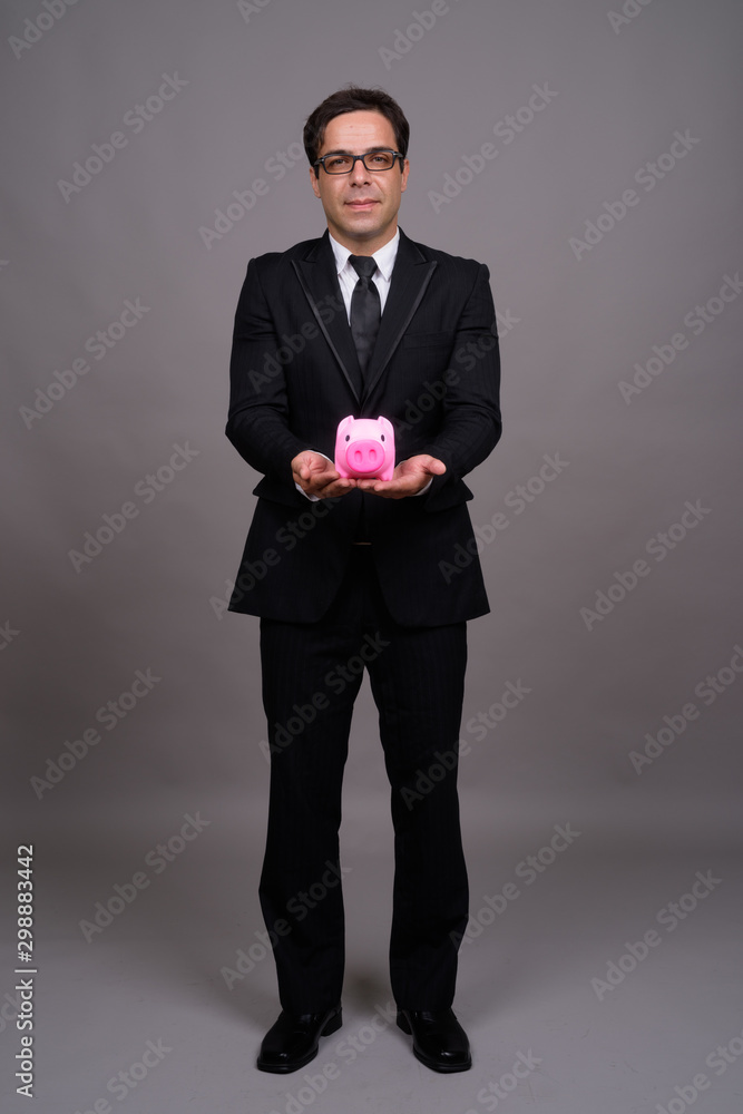 Full body shot of handsome Persian businessman with piggy bank Full body shot of handsome Persian businessman with piggy bank