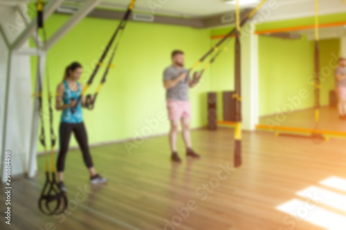 The trainer teaches in the gym to practice a man on the hinges of the TRX while performing an exercise facial thrust, blurred