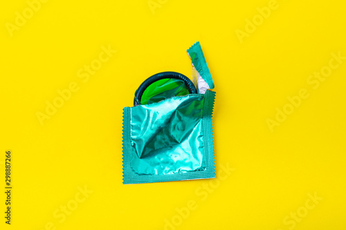 Condom half out of package on a yellow background. A condom use to reduce the probability of pregnancy or sexually transmitted disease (STD). Safe sex and reproductive health concept. photo