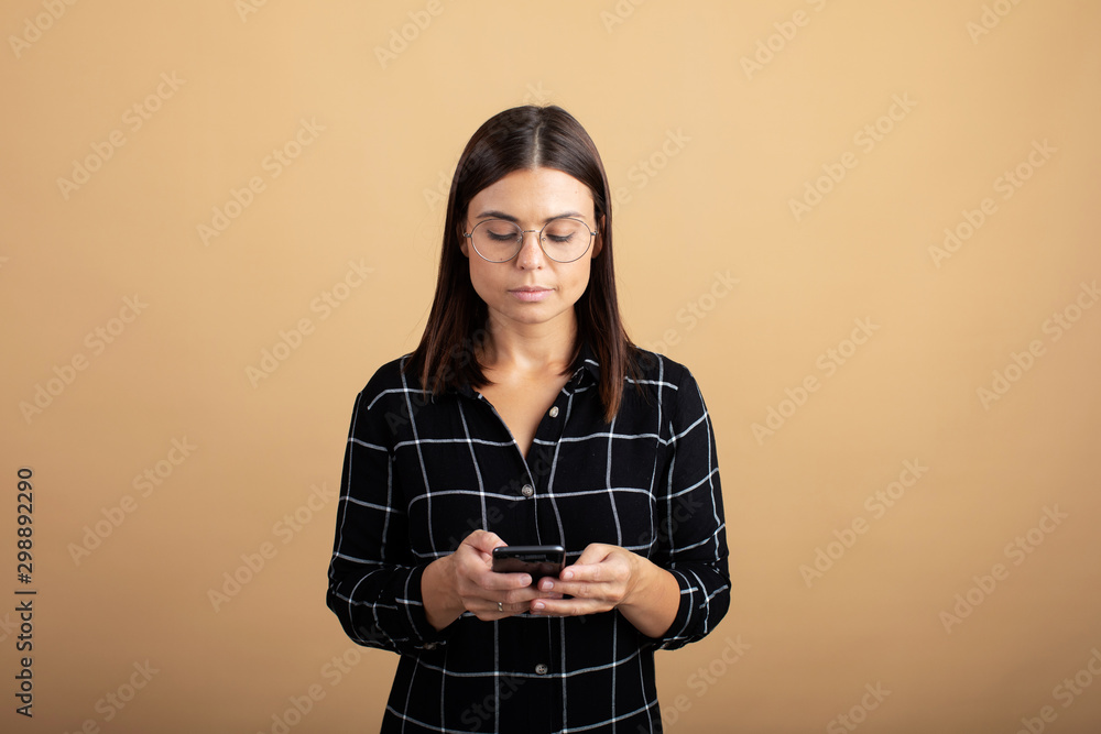 A young woman in a plaid dress stands on an orange background and plays with her phone A young woman in a plaid dress stands on an orange background and plays with her phone