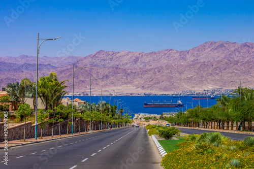 landmark outskirts city park outdoor scenic view of car road down to waterfront port district with cargo ship in Gulf of Aqaba Red sea bay and Jordanian desert mountain background  photo