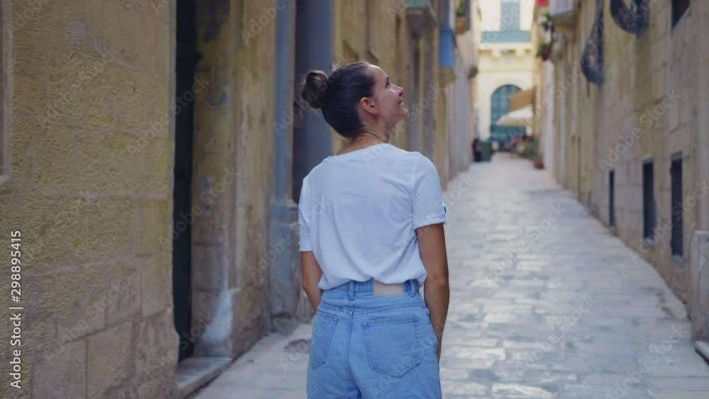 A young woman tourist goes along an old narrow street and considers architecture. Back view A young woman tourist goes along an old narrow street and considers architecture. Back view