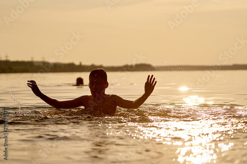 The boy playing in river at sunset. Hands up near the head. Fun and childhood concept.