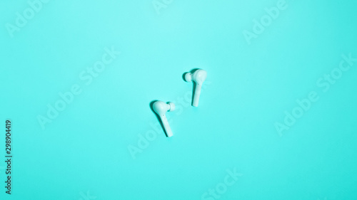 Wireless in ear headphones on blue background close up. Minimal music concept. White earphones flat lay, top view