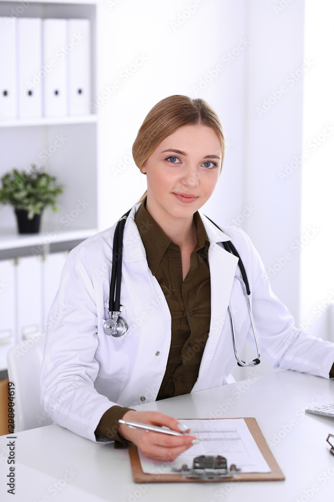 Young woman doctor at work in hospital looking at desktop pc monitor. Physician controls medication history records and exam results. Medicine and healthcare concept Young woman doctor at work in hospital looking at desktop pc monitor. Physician controls medication history records and exam results. Medicine and healthcare concept