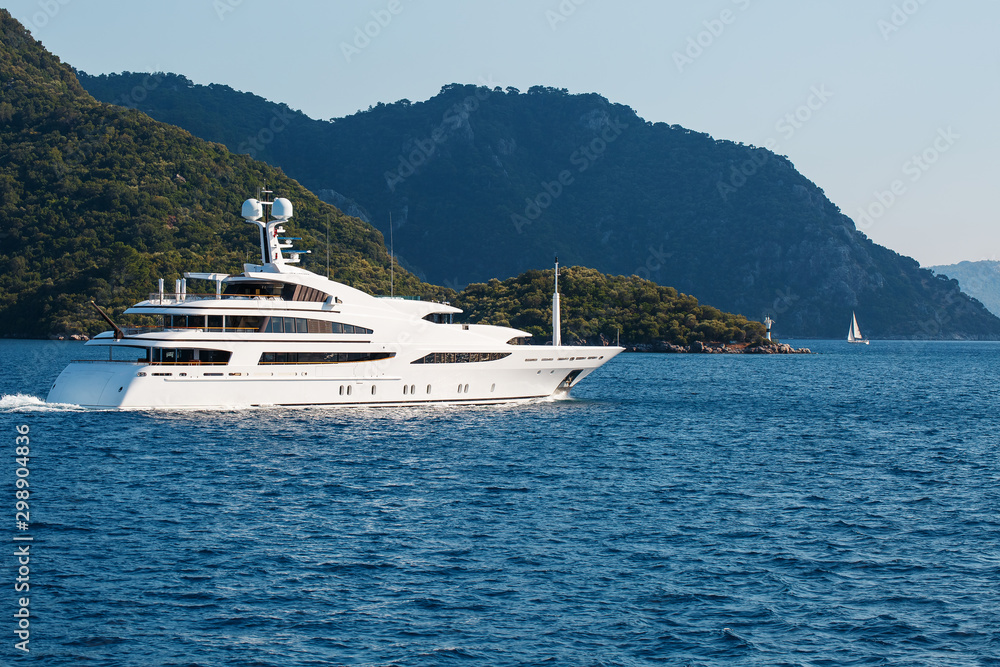 Beautiful modern white yacht with sail on the blue sea, against the backdrop of the mountains.