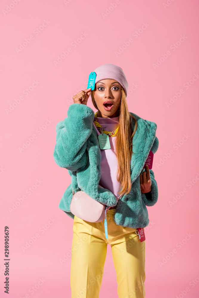 excited, trendy african american woman touching label with sale inscription isolated on pink, fashion doll concept
