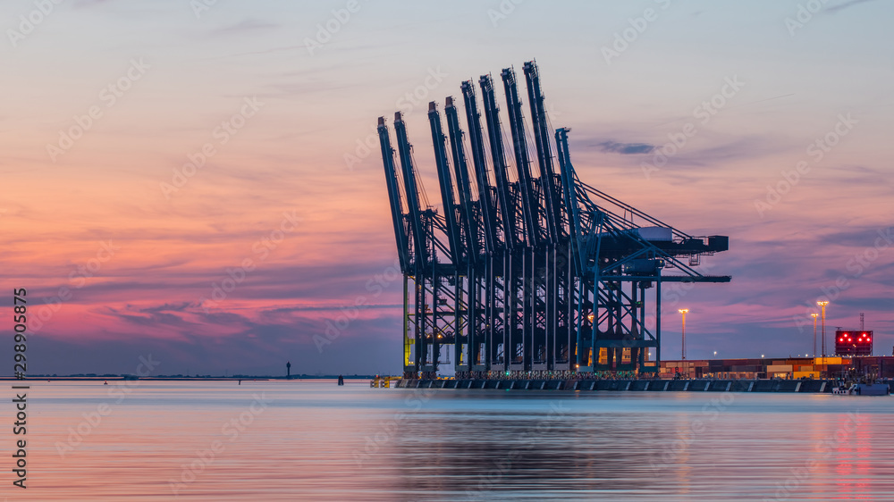 Row of container terminal cranes at red colored sunset in Port of Antwerp, Belgium - obrazy, fototapety, plakaty 