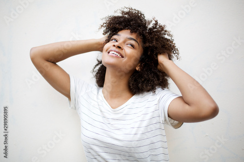 cheerful young african american woman laughing with hand in hair and looking up by white background