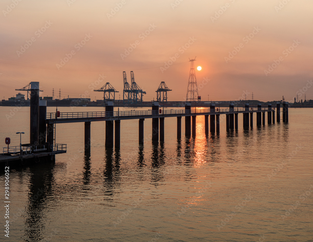 Pier in river Scheldt with container terminal on the background at sunset, Port of Antwerp, Belgium.