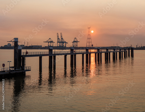 Pier in river Scheldt with container terminal on the background at sunset, Port of Antwerp, Belgium.