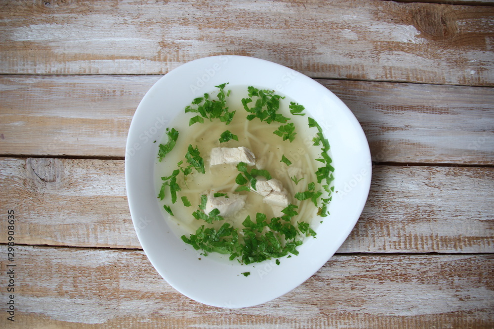 Chiken noodle soup with parsley in white bowl on wooden table Chiken noodle soup with parsley in white bowl on wooden table