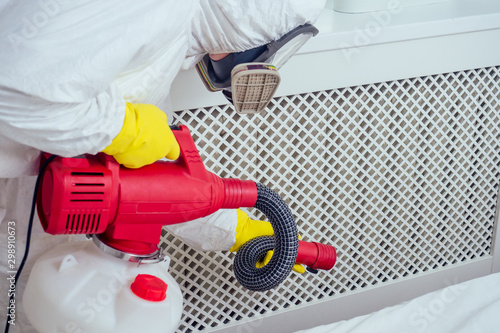 Photos pest control worker lying on floor and spraying pesticides in bedroom