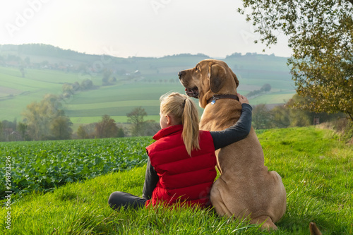 Beste Freunde - ein Mädchen sitzt in der Natur und umarmt seinen besten Freund, einen Broholmer, und beide genießen den Sonnenuntergang 