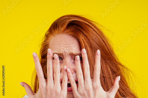 ungroomed nervous unhappy young redhaired ginger woman looking at a broken fingernail and crying .nude manicure in studio yellow background.dry and split ends of hair photo