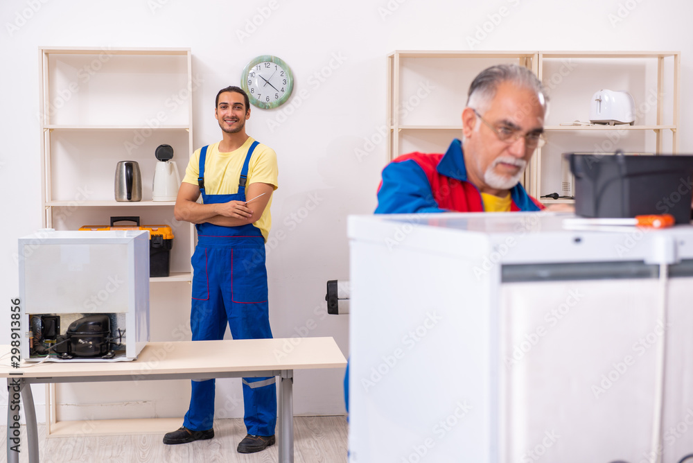 Obraz premium Two contractors repairing fridge at workshop