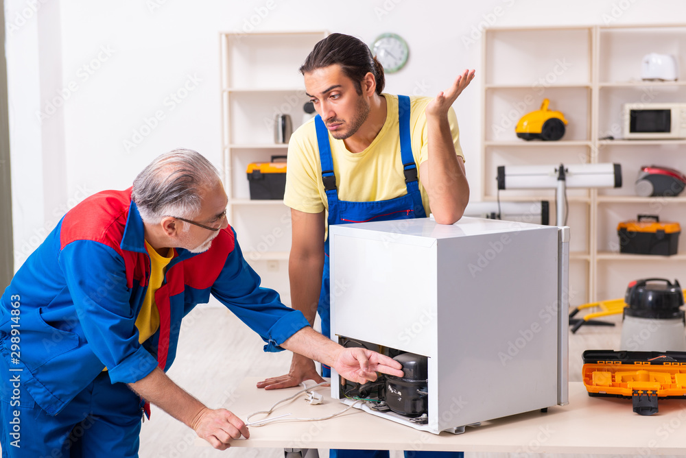 Fototapeta premium Two contractors repairing fridge at workshop