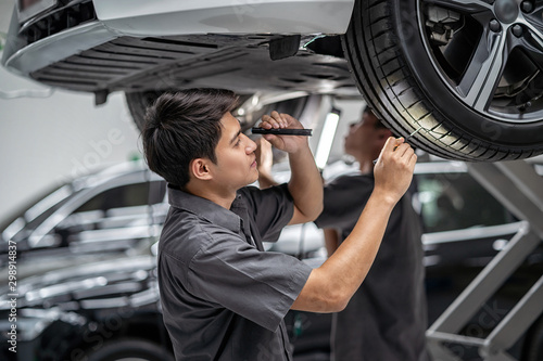 Obraz na płótnie Asian mechanic Checking and torch tire in maintainance service center which is a part of showroom, technician or engineer professional work for customer, car repair concept w salonie