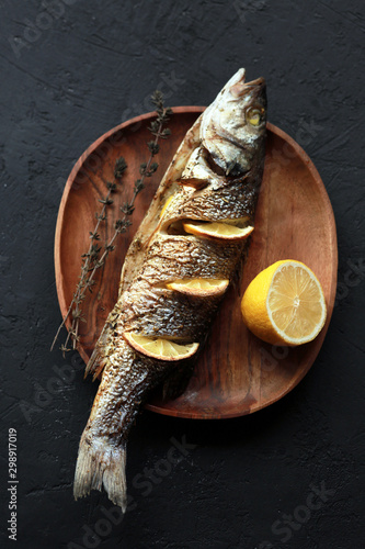  Baked fish with lemon and herbs. Dorado on a plate with vegetables. Tasty fried dorado fish or bream with a gilt head with lemon slices and herbs on a plate, top view, close-up. Place for recipe