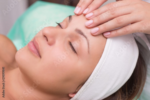 Girl massage therapist does facial massage with a beautiful woman. Hands are closing. Massage room