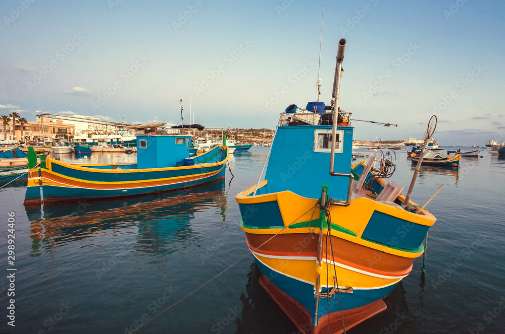 Colorful boats of fishermen in harbor of Malta. Evening over small Mediterranean town