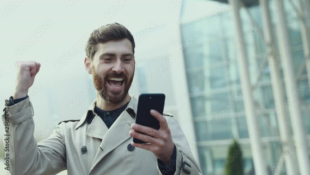 Success and achievement - happy businessman cheering celebrating looking at cell phone. Young urban professional successful business man receiving good news in business. Smartphone app concept Success and achievement - happy businessman cheering celebrating looking at cell phone. Young urban professional successful business man receiving good news in business. Smartphone app concept
