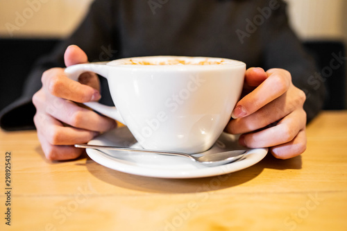 female hands holding a cup of coffee on a wooden table