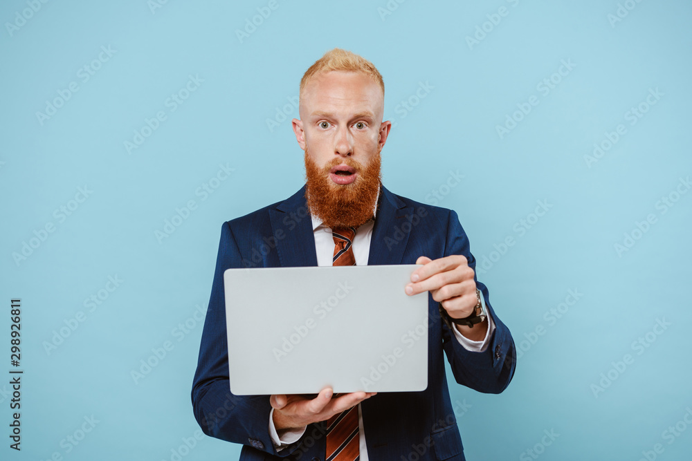 shocked bearded businessman in suit using laptop, isolated on blue shocked bearded businessman in suit using laptop, isolated on blue