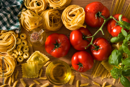 Italian pasta and ingredients. Ravioli, penne pasta, spaghetti, tortellini, tomatoes and basil background