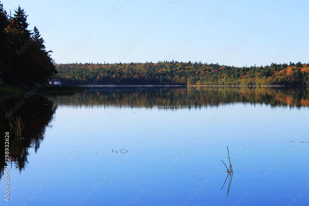 View of shoreline and beach around a lake in autumn, Nova Scotia, Canada. Trees in fall colors. Reflection in the water's surface.
