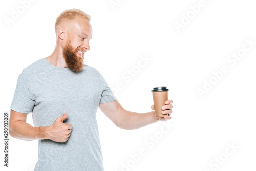 smiling bearded man looking at coffee to go and showing thumb up, isolated on white