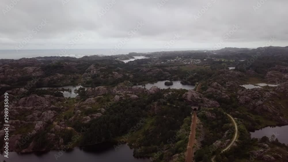 Aerial, tracking, drone shot, over rocky hills, a road and railway tracks, Egersund town, in the background, on a dark, rainy, autumn day, in Rogaland, South Norway Aerial, tracking, drone shot, over rocky hills, a road and railway tracks, Egersund town, in the background, on a dark, rainy, autumn day, in Rogaland, South Norway