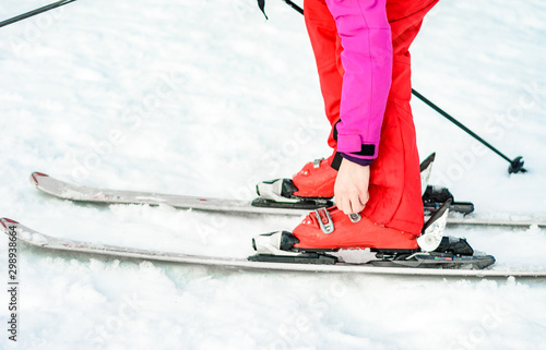 Sport set of skis, boots and sticks in red on woman's leg close up.