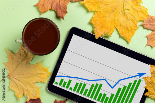 A tablet with a business graph on the desktop. Autumn leaves