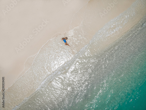 Drone photo of a young pretty girl that is lying on a sandy warm beach during tide.