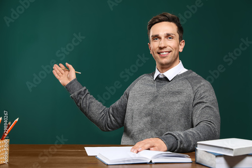 Portrait of male teacher working at table against color background