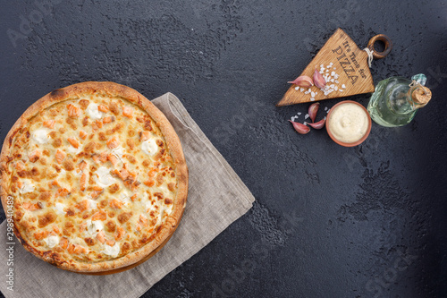 Pizza with salmon and cheese on a textural black background. Closeup. The concept of delicious food. View from above.