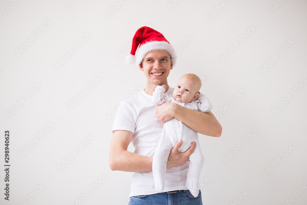 Fototapeta premium My first Christmas. Dad in santa hat holding his baby girl daughter on white background with copy space