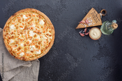 Pizza with salmon and cheese on a textural black background. Closeup. The concept of delicious food. View from above.