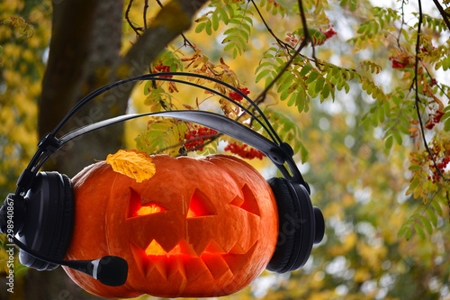 A festive pumpkin with bright glowing eyes and a yellow leaf on the top of its head played music on the radio against the autumn background