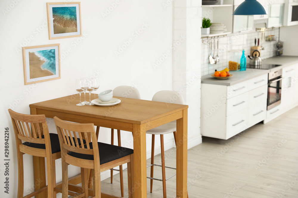 Fototapeta premium Stylish kitchen interior with dining table and bar stools near white wall