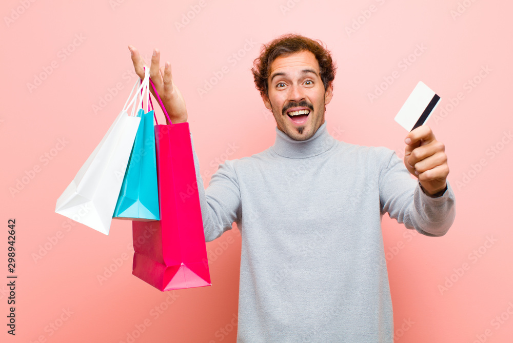 young handsome man with shopping bags against pink flat wall - obrazy, fototapety, plakaty 