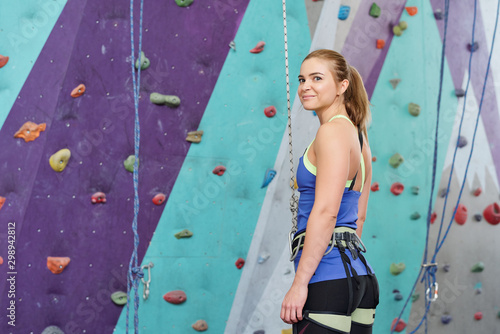 Young blonde woman in special climbing activewear standing by wall
