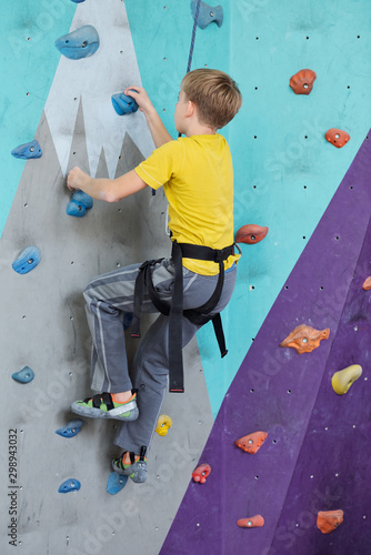Side view of youthful boy in activewear climbing wall while grabbing by rocks