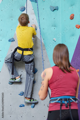 Back view of schoolboy in activewear moving upwards on climbing wall