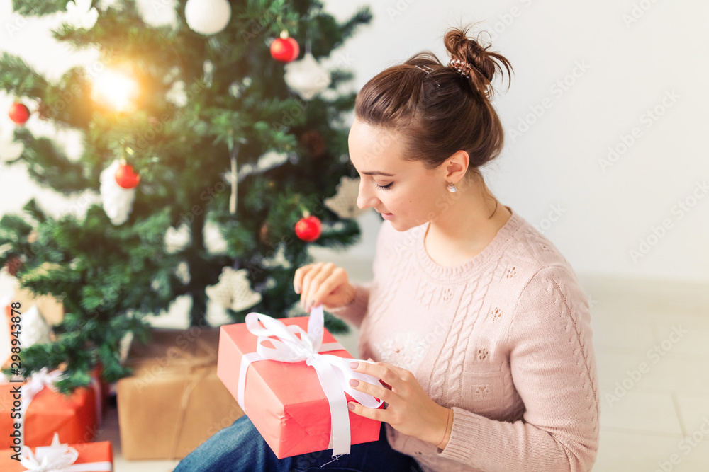 christmas, x-mas, winter, happiness concept - girl opens a gift against the background of the Christmas tree. Happy young woman celebrating Christmas christmas, x-mas, winter, happiness concept - girl opens a gift against the background of the Christmas tree. Happy young woman celebrating Christmas