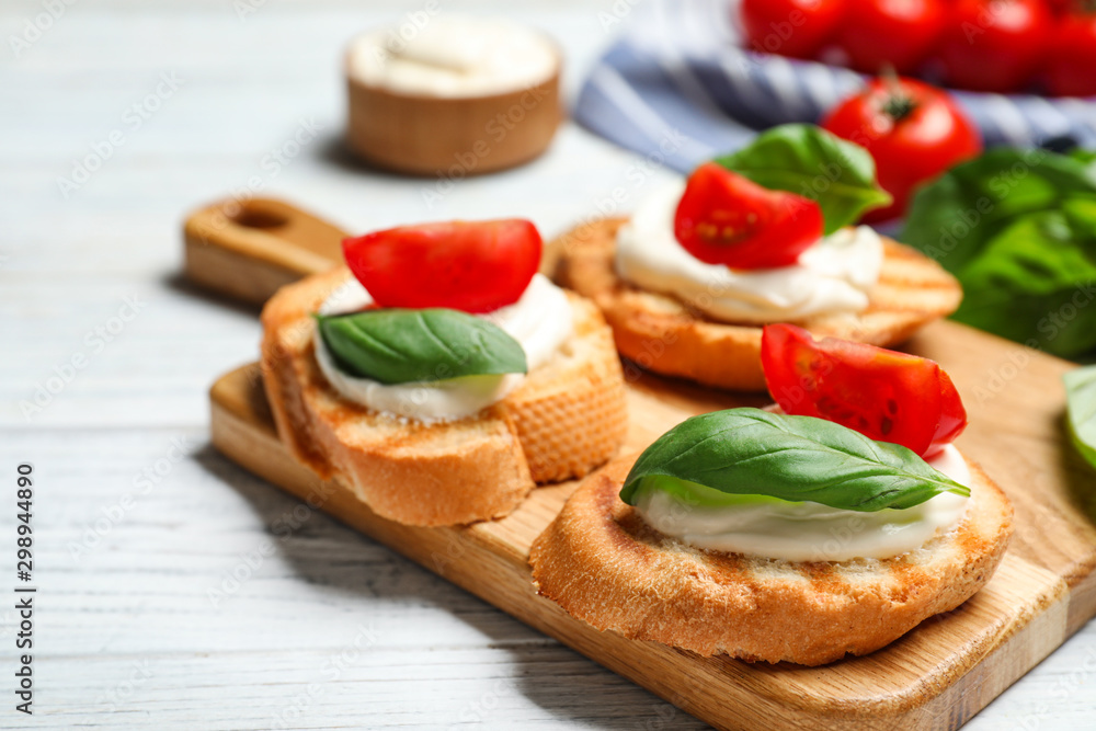 Tasty bruschettas with cheese, basil and tomatoes on white wooden table, closeup