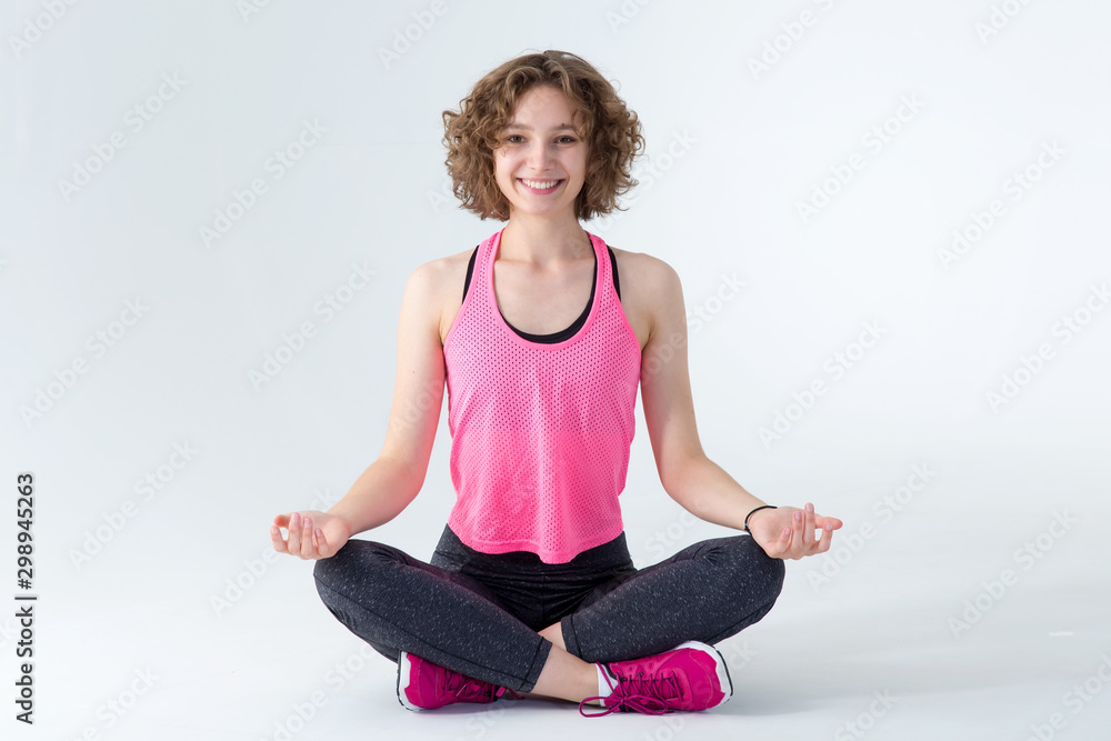 Young fitness woman meditating in lotus position on a gray background. Young fitness woman meditating in lotus position on a gray background.