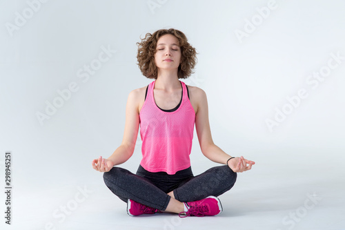 Young fitness woman relaxing after workout. She is meditating in lotus position on a gray background.